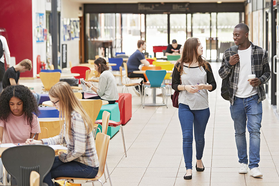 People walk and sit at tables in an open library space with many windows (Photo: ©Monkey Business/Adobe Stock)