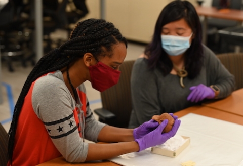 A student handles a terracotta figurine from Ethiopia as Postdoctoral Scholar Denise Lim looks on.