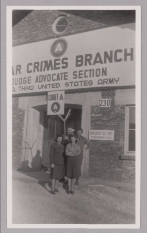 Alt Text Two men and two women (Sylvia and Sylvia) standing in front of a building with the sign War Crimes Branch, Judge Advocate Section; Q. Thurs United States Army; Court A