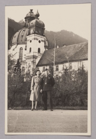 Man and Woman (Jimmy Ualade and Sylvia Mathon) standing together in front of building with mountains behind them