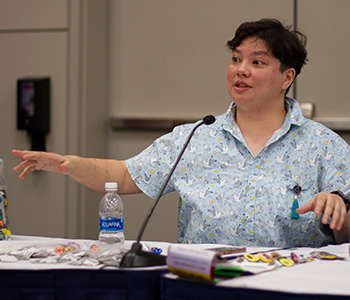 Danielle Costello, science librarian at Louisiana State University in Baton Rouge, speaks to an audience. Game pieces are shown on the table in front of her. 