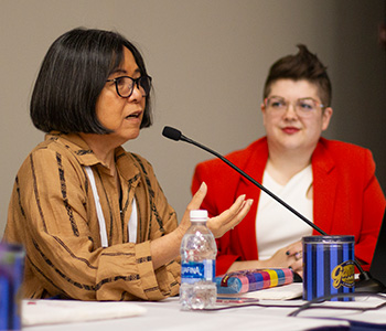 Ling Hwey Jeng, professor and director of the School of Library and Information Studies at Texas Woman’s University in Denton, wears a brown shirt and black glasses while she speaks in front of a microphone.