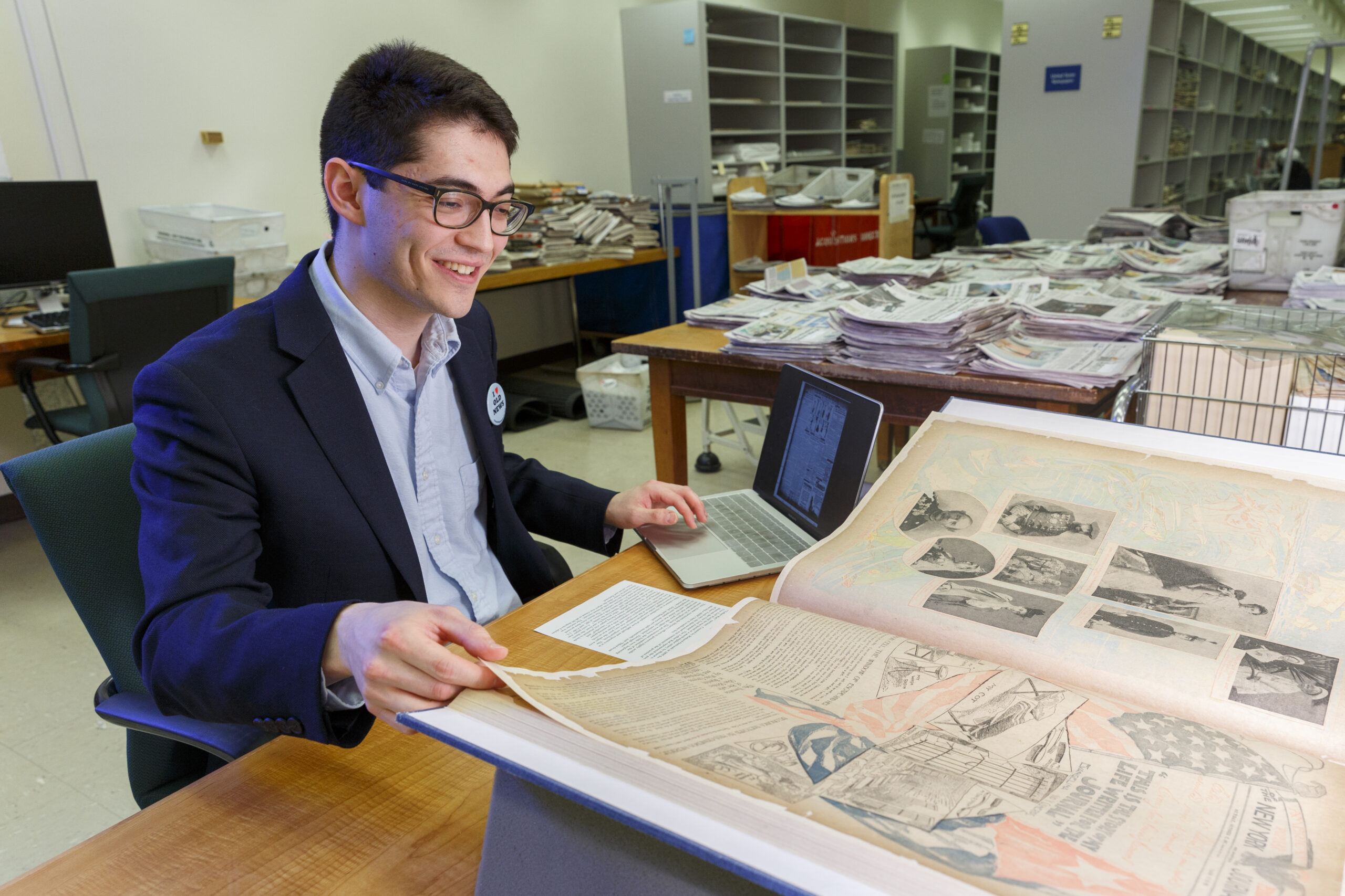 Innovator in Residence Ben Lee sits at a table surrounded by historic newspapers with his laptop at his side.