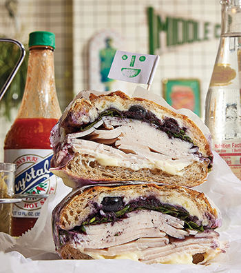 A turkey sandwich and a bottle of hot sauce